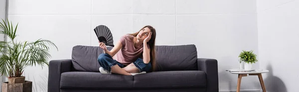 Frustrado joven mujer que sufre de calor y el uso de ventilador de mano en casa, concepto horizontal - foto de stock