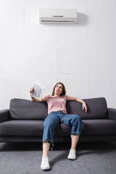 Verärgerte junge Frau leidet unter Hitze und benutzt Zeitung als Handventilator zu Hause mit defekter Klimaanlage — Stockfoto