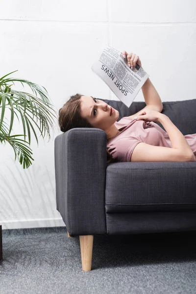 Exhausted woman suffering from heat and using newspaper as hand fan at home — Stock Photo