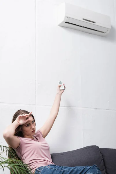 Exhausted girl suffering from heat while trying to switch on air conditioner — Stock Photo