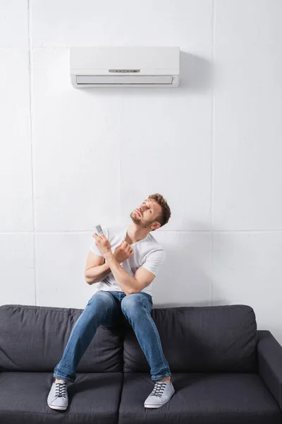 Confused man holding remote controller and suffering from heat with broken air conditioner at home — Stock Photo