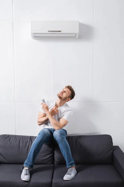 Homem confuso segurando controlador remoto e sofrendo de calor com ar condicionado quebrado em casa — Fotografia de Stock