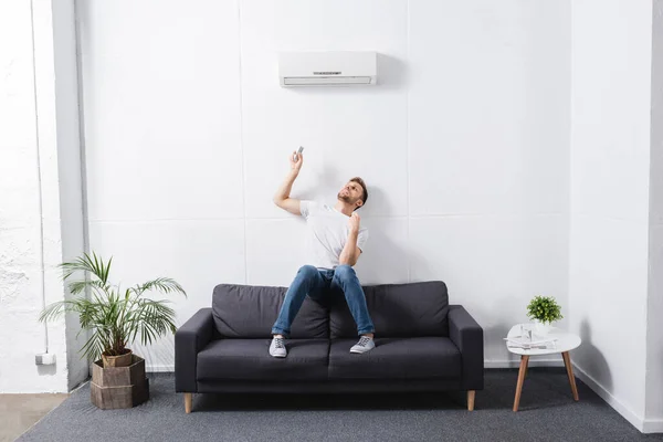 Homme fatigué tenant télécommande et souffrant de chaleur avec climatiseur cassé à la maison — Photo de stock