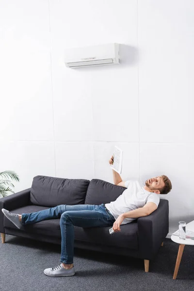 Uomo esausto che soffre di calore durante l'utilizzo di giornale come ventilatore a mano a casa con condizionatore rotto — Foto stock