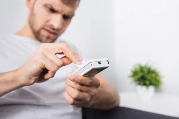 Uomo arrabbiato che cerca di accendere condizionatore d'aria con telecomando a casa, messa a fuoco selettiva — Foto stock
