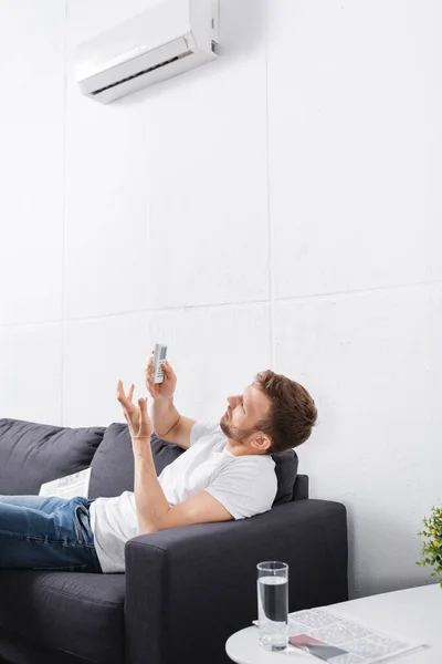 Confused man trying to switch on air conditioner with remote controller at home — Stock Photo