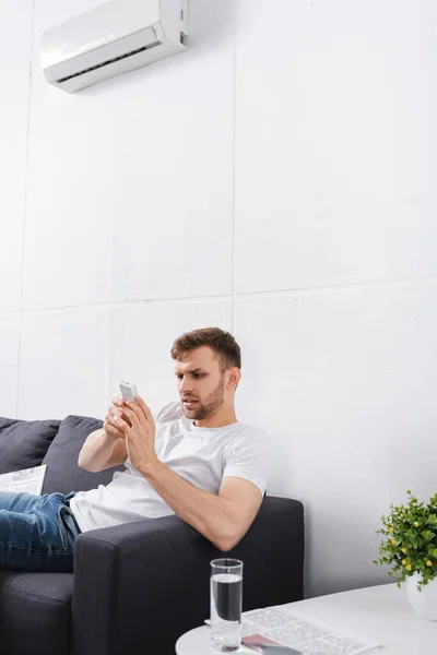 Homem cético tentando ligar ar condicionado com controle remoto em casa — Fotografia de Stock