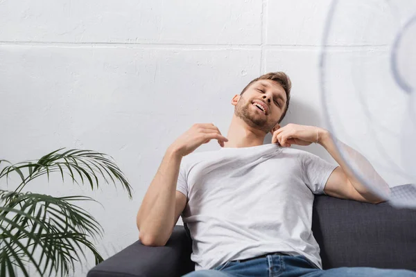 Homme heureux se sentant à l'aise avec ventilateur électrique à la maison pendant la chaleur estivale — Photo de stock