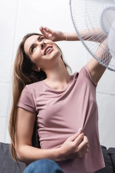 Mulher sorridente sentindo-se confortável com ventilador elétrico em casa durante o calor do verão — Fotografia de Stock