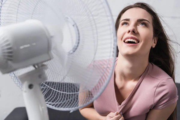 Збуджена жінка відчуває себе комфортно з електричним вентилятором вдома під час літньої спеки — стокове фото