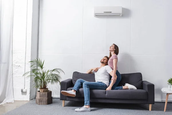 Smiling girlfriend and boyfriend hugging at home with air conditioner — Stock Photo