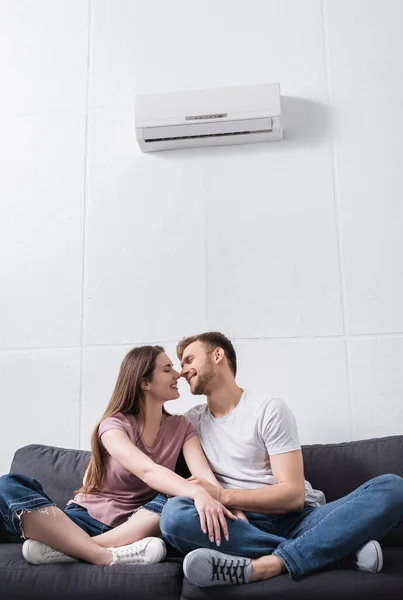 Positive girlfriend and boyfriend hugging and going to kiss at home with air conditioner — Stock Photo