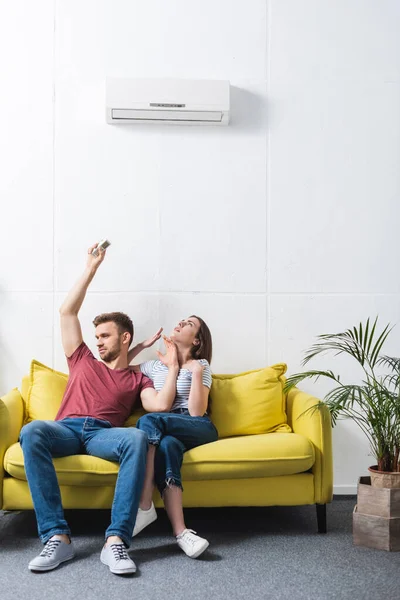 Upset couple with remote controller suffering from heat at home with broken air conditioner — Stock Photo