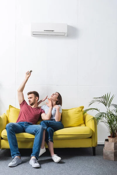 Pareja molesta con mando a distancia que sufre de calor en casa con el aire acondicionado roto - foto de stock