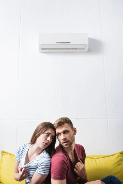 Triste casal sofrendo de calor enquanto sentado em casa com ar condicionado quebrado — Fotografia de Stock