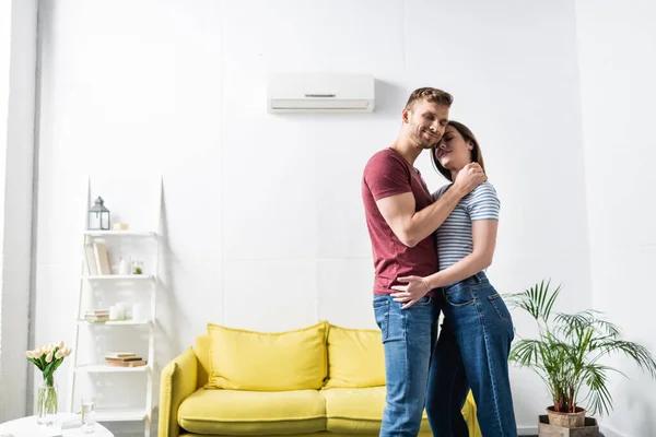 Sonriente pareja abrazándose en casa con aire acondicionado - foto de stock