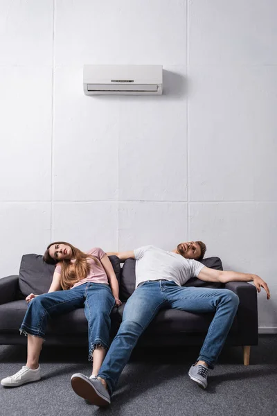 Couple épuisé souffrant de chaleur tout en étant assis à la maison avec climatiseur cassé — Photo de stock