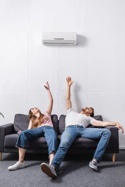 Couple épuisé souffrant de chaleur tout en étant assis à la maison avec climatiseur cassé — Photo de stock