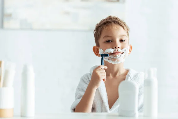 Foco seletivo de menino bonito barbear no banheiro perto de produtos de higiene pessoal — Fotografia de Stock