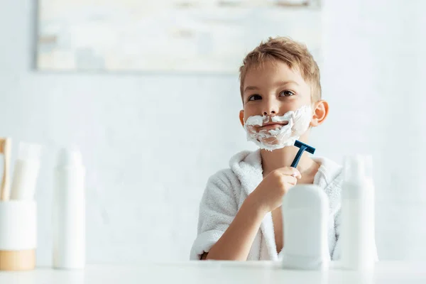 Foco seletivo de menino bonito barbear no banheiro perto de produtos de higiene pessoal — Fotografia de Stock