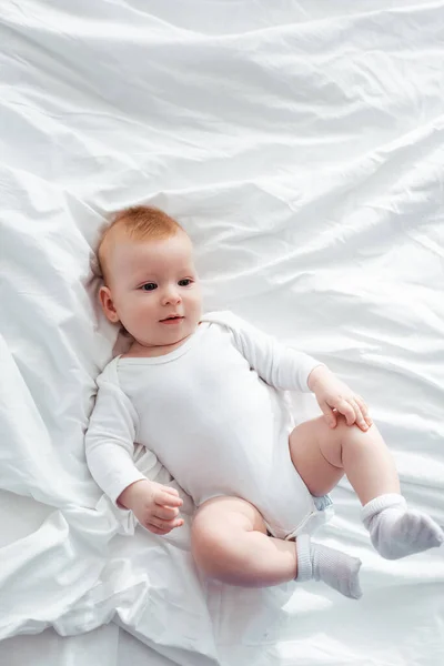 Blick von oben auf entzückende kleine Jungen im Strampler, die auf Bettwäsche liegen und wegschauen — Stockfoto