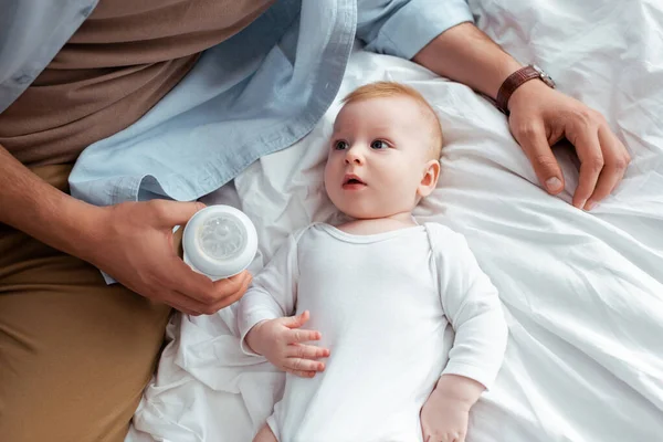 Cropped view of man holding baby bottle with milk near adorable little son — Stock Photo