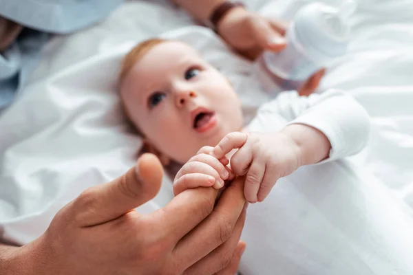 Selective focus of cute infant touching fathers hands while lying in bed — Stock Photo