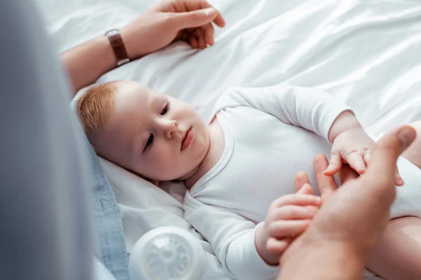 Vista de ángulo alto del adorable bebé niño tocando la mano de los padres mientras está acostado en la cama - foto de stock