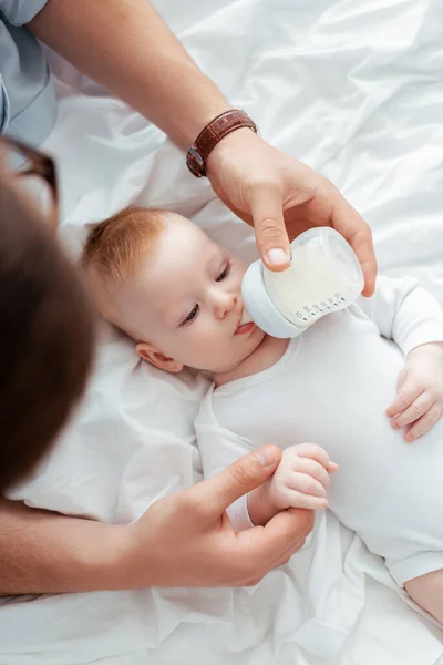 Visão aérea do menino bebendo leite de mamadeira em mãos dos pais — Fotografia de Stock