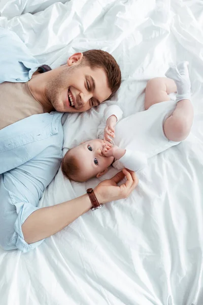 Jeune père joyeux touchant adorable petit fils tout en étant couché près de lui dans son lit — Photo de stock