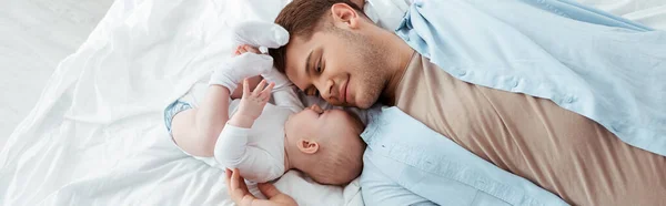 Top view of happy father lying on bed face to face with cute baby boy, panoramic shot — Stock Photo
