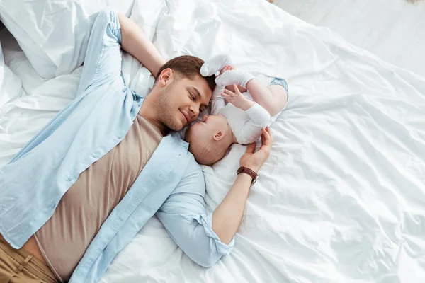 Top view of happy father lying on bed face to face with cute baby boy — Stock Photo