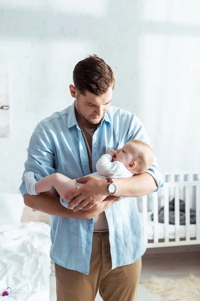 Handsome young man holding cute little son on hands in bedroom — Stock Photo