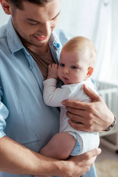 Happy young father holding cute baby boy in romper on hands — Stock Photo