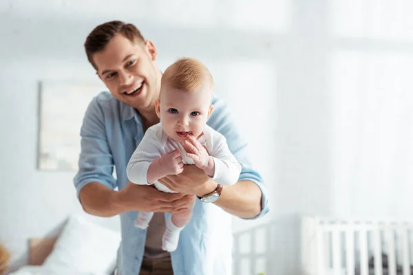 Lindo bebé chico mirando cámara en manos de feliz padre - foto de stock