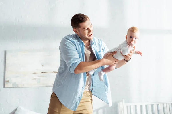 Excited young man holding baby in outstretched hands in bedroom — Stock Photo