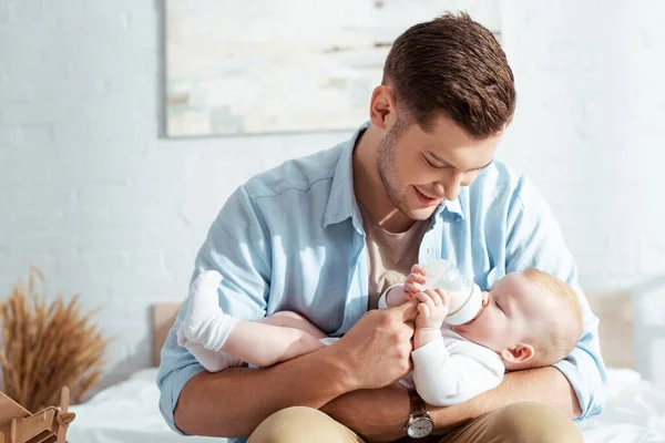 Feliz joven padre alimentación lindo bebé niño con leche de biberón - foto de stock