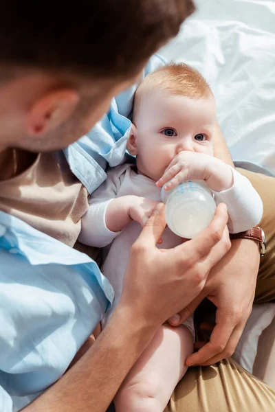 High angle view of man feeding cute baby boy with milk from baby bottle — Stock Photo