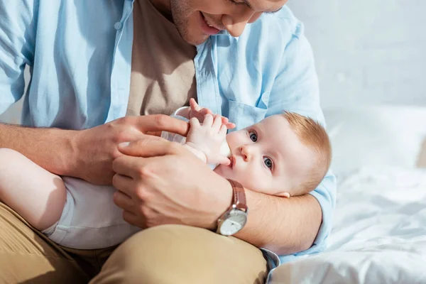 Recortado vista de sonriente padre alimentación adorable hijo con leche de biberón - foto de stock