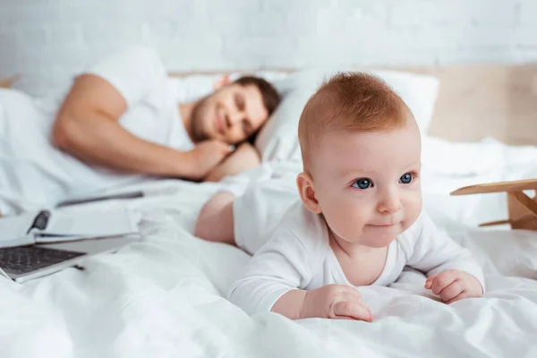 Selective focus of happy father resting while cute little son crawling on bed — Stock Photo