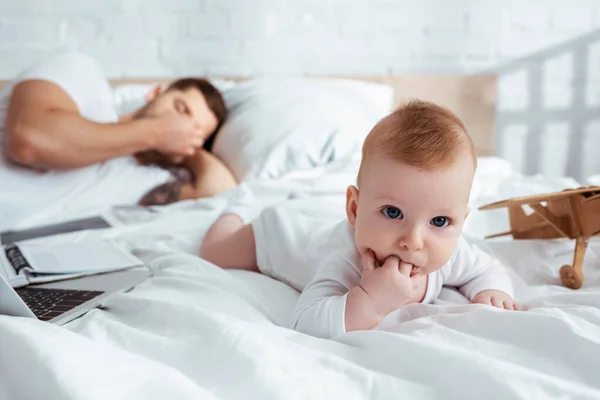 Selective focus of cute infant crawling on bed neat tired father — Stock Photo