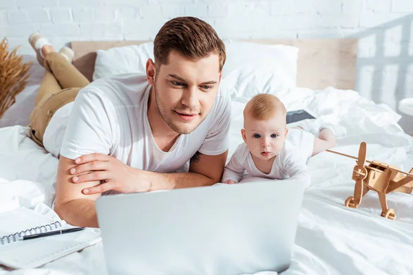Enfoque selectivo de padre e hijo mirando portátil en la cama cerca de avión de juguete - foto de stock
