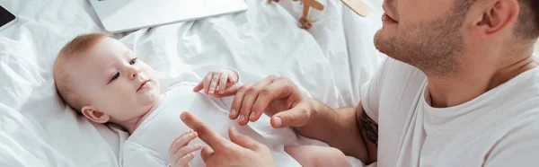 Ausgeschnittene Ansicht eines jungen Vaters, der Hände eines entzückenden Säuglings berührt, horizontales Bild — Stockfoto