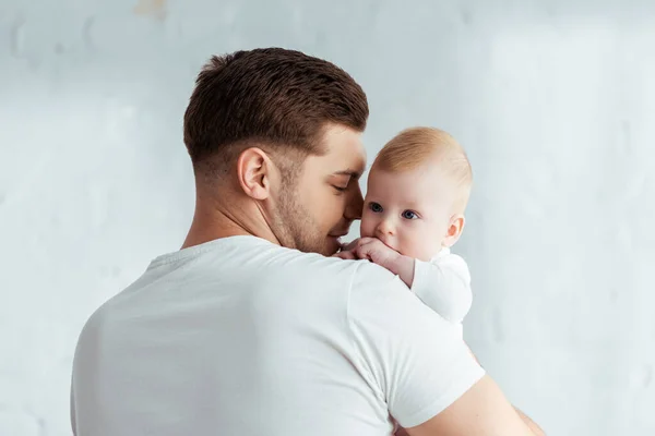 Felice giovane uomo che tiene adorabile bambino sulle mani in camera da letto — Foto stock