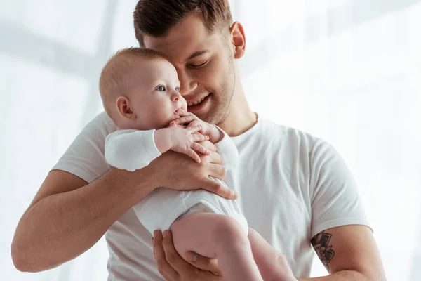 Feliz padre sosteniendo y abrazando adorable bebé niño con los ojos cerrados - foto de stock