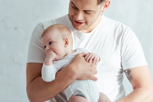 Adorable bébé garçon tenant la main dans la bouche tout en étant assis sur les mains des pères — Photo de stock