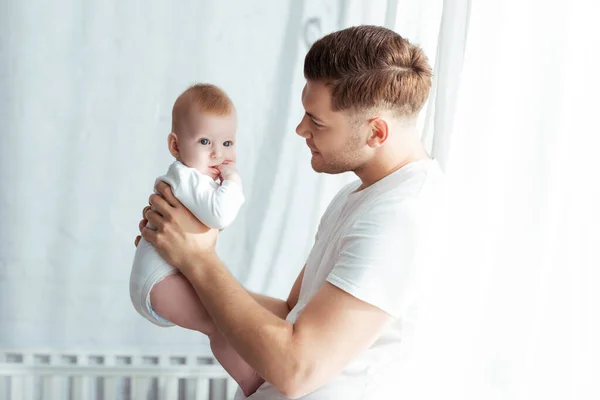 Jeune père regardant adorable bébé garçon tout en le tenant dans la chambre — Photo de stock