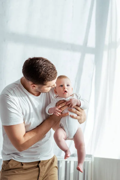 Young father holding cute baby boy in body romper on hands — Stock Photo