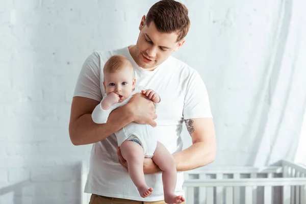 Young father holding adorable infant in romper on hands in bedroom — Stock Photo