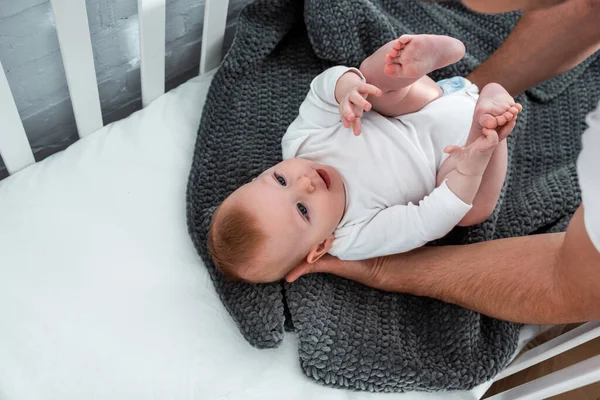 Cropped view of man touching cute baby boy lying in baby cot on blanket — Stock Photo